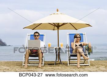 Picture - couple using laptop 
and phone on beach. 
fotosearch - search 
stock photos, 
pictures, images, 
and photo clipart