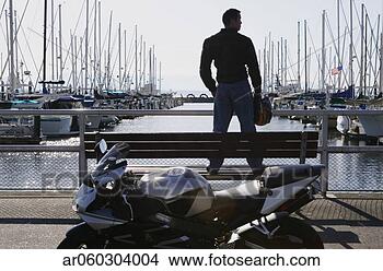 Stock Photo - rear view of a 
young man standing 
in front of a 
motorcycle at 
a dock. fotosearch 
- search stock 
photos, pictures, 
images, and photo 
clipart