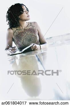 Picture - woman seated at 
a table with a 
notebook and a 
pen looking at 
the side. fotosearch 
- search stock 
photos, pictures, 
images, and photo 
clipart