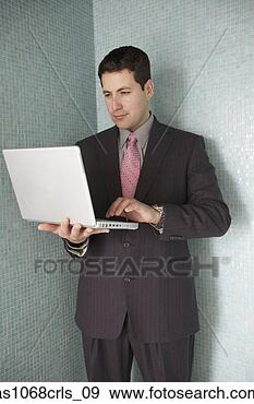Stock Photograph - hispanic businessman 
standing in a 
corner using his 
laptop. fotosearch 
- search stock 
photos, pictures, 
images, and photo 
clipart