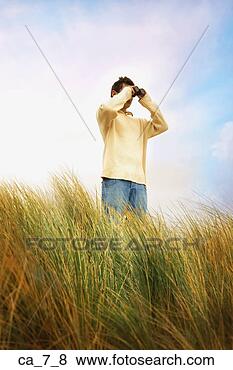 Stock Photo - man standing in 
dune grass using 
binoculars. fotosearch 
- search stock 
photos, pictures, 
images, and photo 
clipart