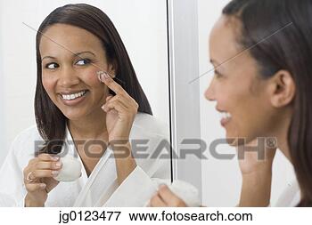 Picture - african woman 
applying face 
cream in mirror. 
fotosearch - search 
stock photos, 
pictures, images, 
and photo clipart