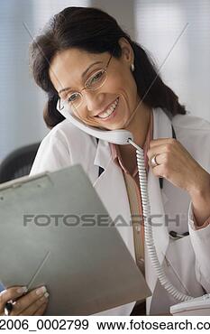 Stock Photograph - female doctor 
talking on the 
phone while examining 
clipboard. fotosearch 
- search stock 
photos, pictures, 
images, and photo 
clipart