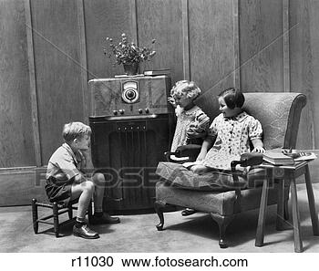 Stock Photography - 1930s pair of 
girls & boy sitting 
in living room 
listening to radio. 
fotosearch - search 
stock photos, 
pictures, images, 
and photo clipart