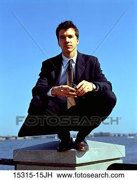Stock Photo - young businessman 
with cellphone, 
 squatting on 
railing column 
at. fotosearch 
- search stock 
photos, pictures, 
images, and photo 
clipart