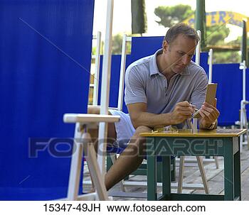 Stock Photo - prime man using 
pda,  sitting 
in lounge chair 
at outdoor cafe. 
fotosearch - search 
stock photos, 
pictures, images, 
and photo clipart
