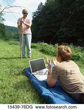 Stock Photo - young man lying 
on grass by pond, 
 using laptop 
and talking to 
mature. fotosearch 
- search stock 
photos, pictures, 
images, and photo 
clipart