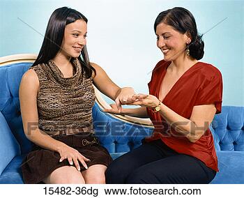 Stock Photo - two latinas sitting 
on a couch next 
to each other, 
 one showing a. 
fotosearch - search 
stock photos, 
pictures, images, 
and photo clipart