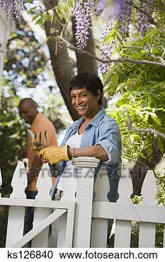 Stock Photography - woman standing 
by fence with 
gardening equipment. 
fotosearch - search 
stock photos, 
pictures, images, 
and photo clipart