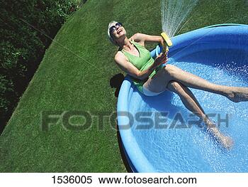 Stock Image - mature woman sits 
in a paddling 
pool spraying 
water from a hosepipe. 
fotosearch - search 
stock photos, 
pictures, images, 
and photo clipart