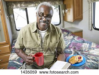 Stock Photograph - senior man sits 
on a bed in a 
motor home,  having 
a snack and reading. 
fotosearch - search 
stock photos, 
pictures, images, 
and photo clipart
