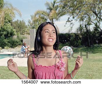 Picture - smiling teenage 
girl stands in 
a garden listening 
to music on her. 
fotosearch - search 
stock photos, 
pictures, images, 
and photo clipart