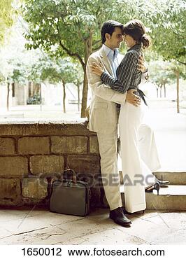 Stock Photo - well-dressed couple 
stand embracing 
by a stone wall 
in a park. fotosearch 
- search stock 
photos, pictures, 
images, and photo 
clipart