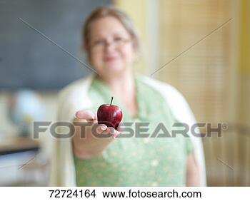 Stock Photo - mature female 
teacher holding 
out apple in hand 
(focus on apple). 
fotosearch - search 
stock photos, 
pictures, images, 
and photo clipart
