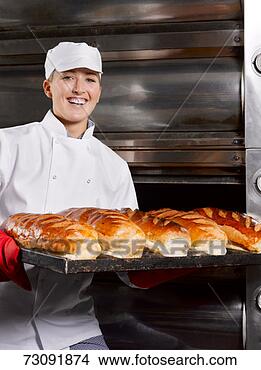 Stock Photo - female baker carrying 
tray of fresh 
breads in bakery, 
portrait. fotosearch 
- search stock 
photos, pictures, 
images, and photo 
clipart