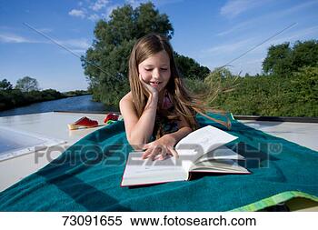 Stock Image - girl (8-9) lying 
on blanket by 
waterreading book. 
fotosearch - search 
stock photos, 
pictures, images, 
and photo clipart