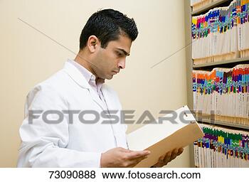 Stock Photo - male doctor reading 
file by filing 
cabinet. fotosearch 
- search stock 
photos, pictures, 
images, and photo 
clipart