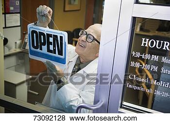 Stock Photo - senior male pharmacist 
hanging 'open' 
sign in shop door, 
elevated view. 
fotosearch - search 
stock photos, 
pictures, images, 
and photo clipart