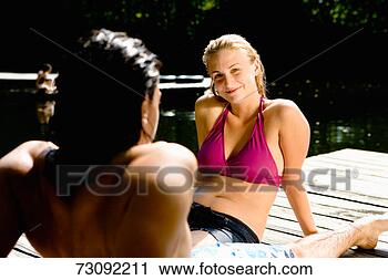 Stock Photography - young couple in 
swimwear, sitting 
on jetty. fotosearch 
- search stock 
photos, pictures, 
images, and photo 
clipart