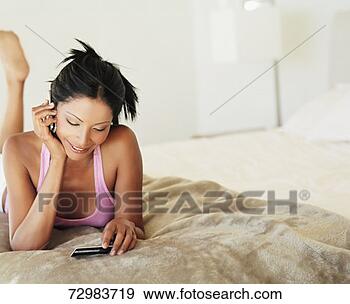 Stock Photograph - young woman lying 
on bed using mobile 
phone. fotosearch 
- search stock 
photos, pictures, 
images, and photo 
clipart