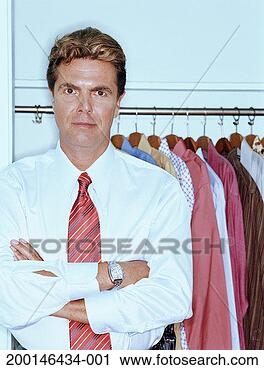 Stock Photography - man standing in 
front of clothes 
rack, arms crossed, 
portrait. fotosearch 
- search stock 
photos, pictures, 
images, and photo 
clipart