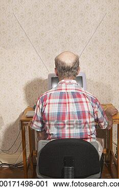 Stock Photography - senior man sitting 
at desk, using 
computer, rear 
view. fotosearch 
- search stock 
photos, pictures, 
images, and photo 
clipart