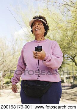 Stock Photography - senior woman wearing 
headphones, exercising 
in park, smiling. 
fotosearch - search 
stock photos, 
pictures, images, 
and photo clipart