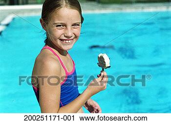 Stock Photography - girl (7-9) eating 
ice cream bar 
beside swimming 
pool, smiling. 
fotosearch - search 
stock photos, 
pictures, images, 
and photo clipart