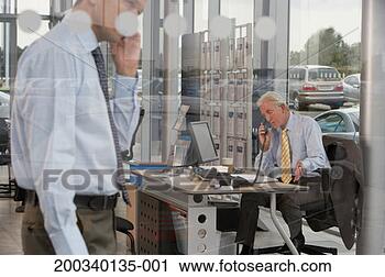 Stock Photography - salesman using 
phone at desk 
in car showroom, 
man in foreground. 
fotosearch - search 
stock photos, 
pictures, images, 
and photo clipart