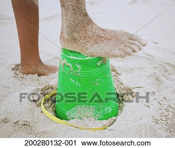 Stock Photography - girl (10-12) with 
sandy foot on 
plastic bucket 
at beach, low 
section. fotosearch 
- search stock 
photos, pictures, 
images, and photo 
clipart