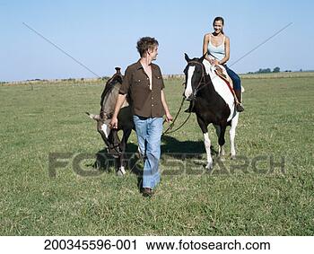 Stock Photography - young man leading 
young woman and 
horses across 
field. fotosearch 
- search stock 
photos, pictures, 
images, and photo 
clipart