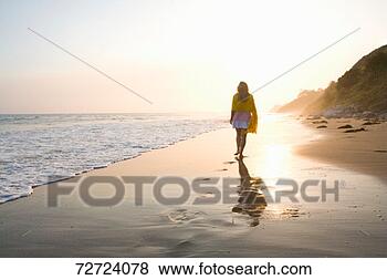 Stock Photo - woman walking 
across wet sand 
on beach, sunset. 
fotosearch - search 
stock photos, 
pictures, images, 
and photo clipart