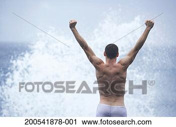 Stock Photography - man standing in 
front of crashing 
wave, arms raised, 
rear view. fotosearch 
- search stock 
photos, pictures, 
images, and photo 
clipart