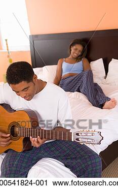 Stock Photography - mature man and 
young woman sitting 
on bed, man playing 
acoustic guitar. 
fotosearch - search 
stock photos, 
pictures, images, 
and photo clipart