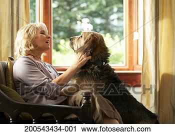 Stock Photography - mature woman sitting 
on armchair, petting 
dog, side view. 
fotosearch - search 
stock photos, 
pictures, images, 
and photo clipart