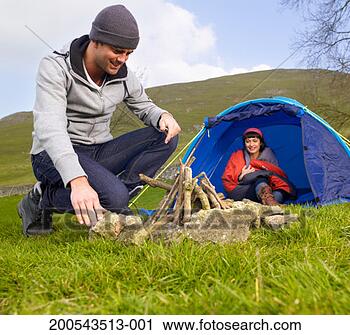 Stock Photography - young man preparing 
campfire while 
woman in tent 
watches. fotosearch 
- search stock 
photos, pictures, 
images, and photo 
clipart