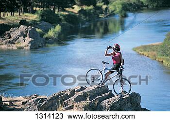 Stock Photo - woman standing 
on top of a rock 
drinking from 
a water bottle 
and. fotosearch 
- search stock 
photos, pictures, 
images, and photo 
clipart