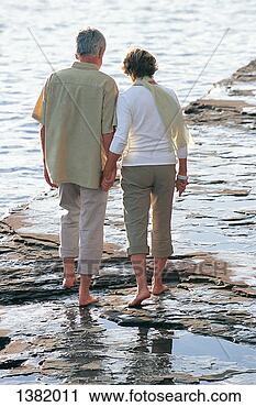 Stock Photography - rear view of a 
senior couple 
walking along 
a rugged, rocky 
coastline. fotosearch 
- search stock 
photos, pictures, 
images, and photo 
clipart
