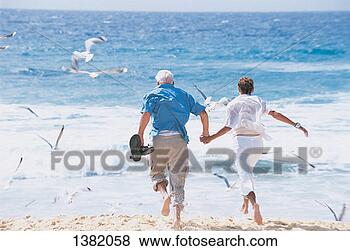 Stock Photo - rear view of a 
senior couple 
running towards 
the sea. fotosearch 
- search stock 
photos, pictures, 
images, and photo 
clipart