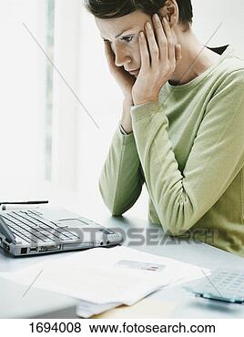 Stock Photo - anxious woman 
sits at a desk 
using a laptop 
and paying a bill 
online. fotosearch 
- search stock 
photos, pictures, 
images, and photo 
clipart