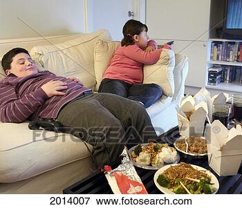Picture - overweight brother 
and sister sitting 
on a sofa eating 
takeaway food. 
fotosearch - search 
stock photos, 
pictures, images, 
and photo clipart