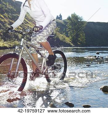 Foto - mulher, montando, 
montanha, bicicleta, 
através, rio. 
fotosearch - busca 
de fotos, imagens 
e clipart