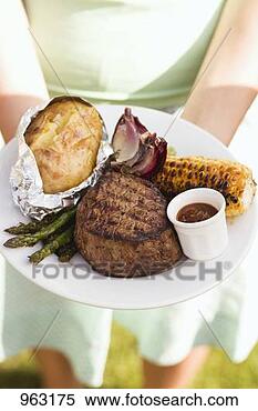 Stock Image - woman holding 
a plate of grilled 
steak and accompaniments. 
fotosearch - search 
stock photos, 
pictures, images, 
and photo clipart