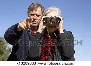 Stock Photo - senior man pointing 
beside senior 
woman looking 
through binoculars. 
fotosearch - search 
stock photos, 
pictures, images, 
and photo clipart