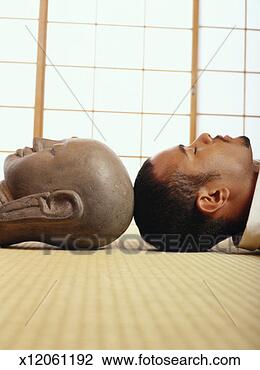 Stock Photo - man lying beside 
stone buddha statue, 
side view. fotosearch 
- search stock 
photos, pictures, 
images, and photo 
clipart