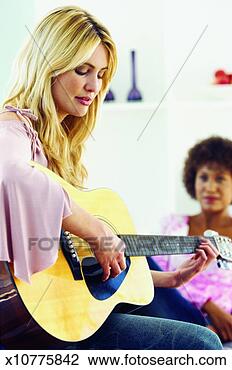 Stock Photo - close-up of young 
woman playing 
guitar with other 
woman in background. 
fotosearch - search 
stock photos, 
pictures, images, 
and photo clipart