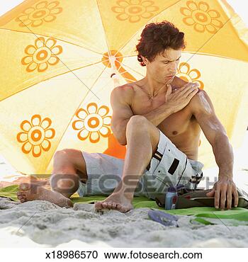 Stock Photography - mid adult man 
applying suntan 
lotion under a 
beach umbrella. 
fotosearch - search 
stock photos, 
pictures, images, 
and photo clipart