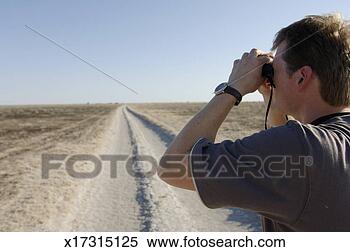 Stock Image - man standing on 
dirt track, looking 
through binoculars, 
side view. fotosearch 
- search stock 
photos, pictures, 
images, and photo 
clipart