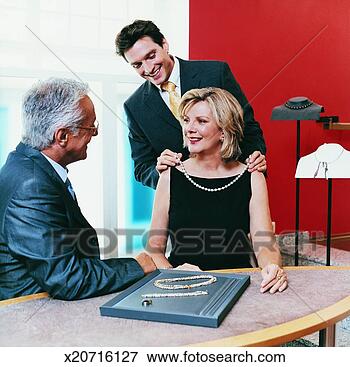 Picture - shop assistant 
helping a woman 
to wear a pearl 
necklace in a. 
fotosearch - search 
stock photos, 
pictures, images, 
and photo clipart