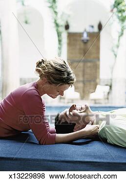 Stock Photo - woman pampering 
a realxed man 
lying on a matress 
in a courtyard. 
fotosearch - search 
stock photos, 
pictures, images, 
and photo clipart